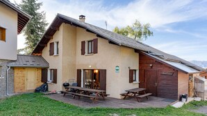 Un chalet de dos pisos con un patio, contraventanas de madera y un letrero que indica que es una casa de huéspedes rural.