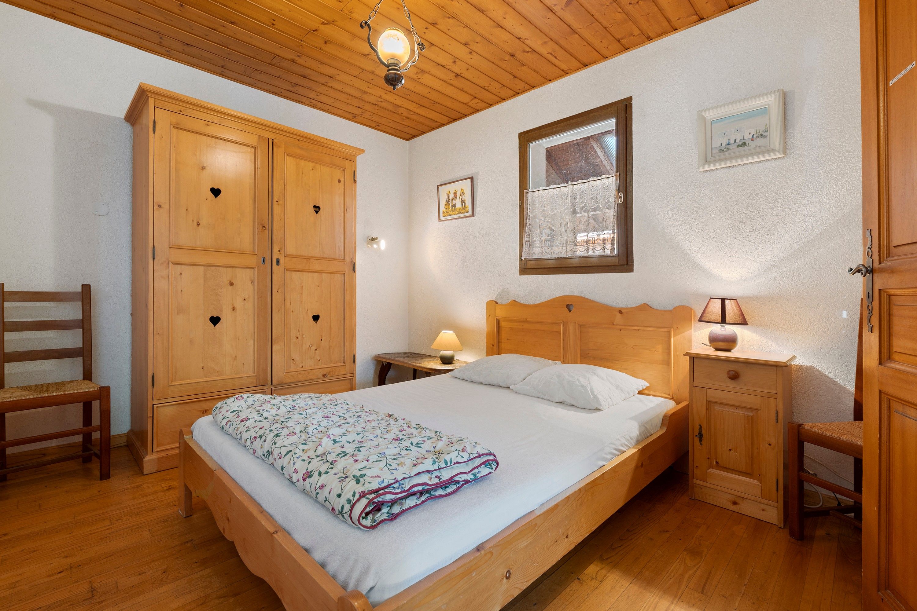 Een slaapkamer met een houten bed, een nachtkastje met een lamp, een houten kledingkast en een stoel.
