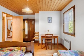 Habitación con cama, escritorio, silla, piso de madera, radiador y ventana con vistas.