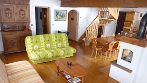 Una sala de estar con sofá, un sofá de color verde y estampado, una mesa de centro de madera, una mesa de comedor con sillas, una escalera y una zona de cocina.