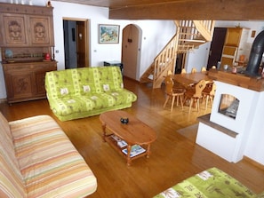 En stue med sofa, en sofa med grønt mønster, et træsofabord, et spisebord med stole, en trappe og et køkkenområde.