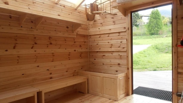 Un sauna de madera con bancos, un asiento en banco, un armario pequeño y un tragaluz.