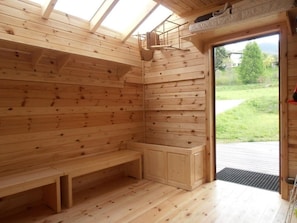 Et træs sauna med bænke, et siddeområde, et lille skab og et ovenlys.