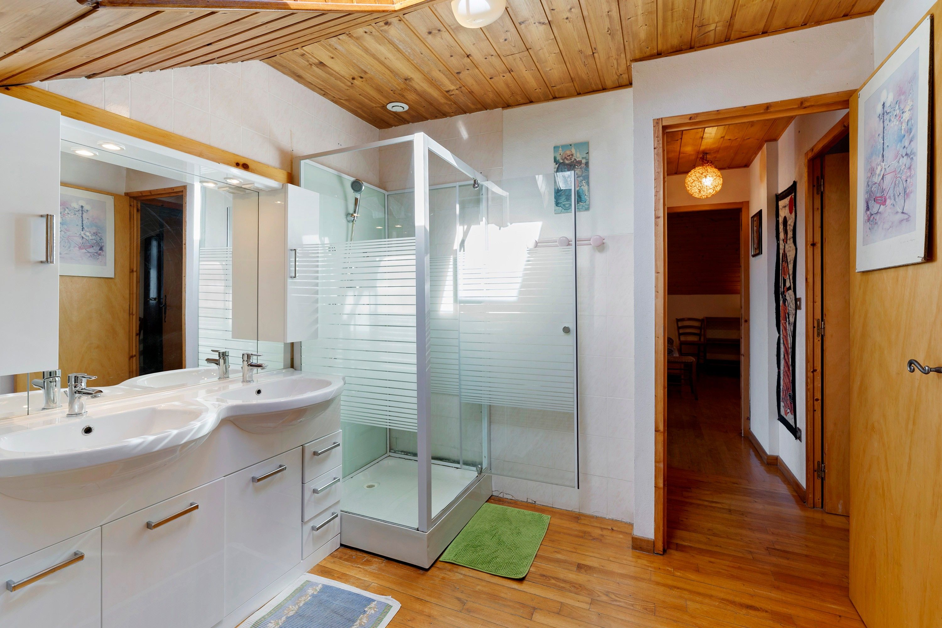 Un baño moderno con cabina de ducha de vidrio, muebles de color blanco y techo de madera.