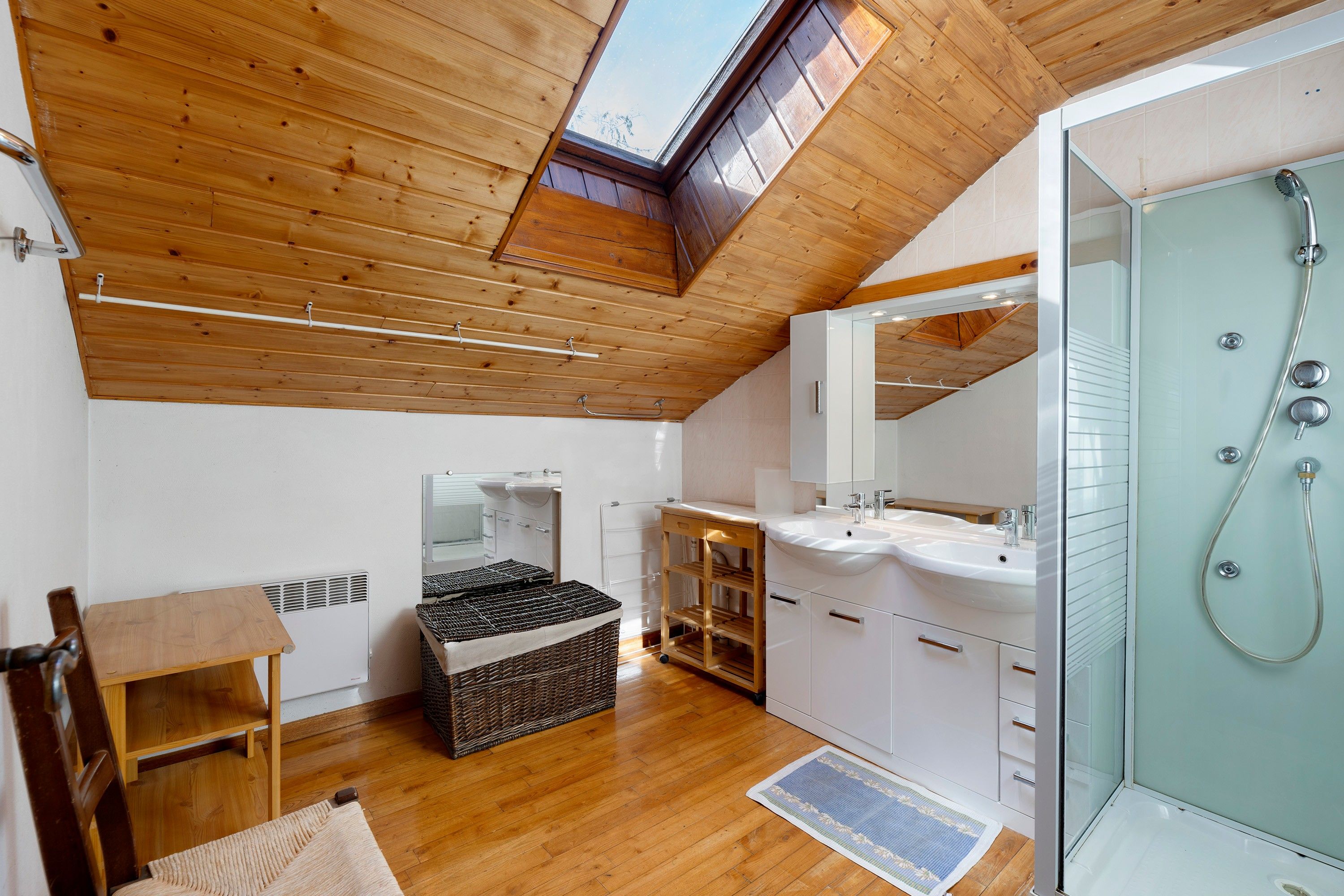 A modern bathroom with a skylight, a glass shower enclosure, and wooden flooring.
