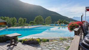 Un área de piscina con terraza de madera, un banco y vistas a montañas.