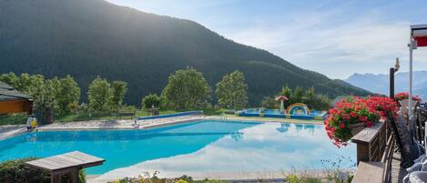 A pool area with a wooden deck, a bench, and a view of mountains.