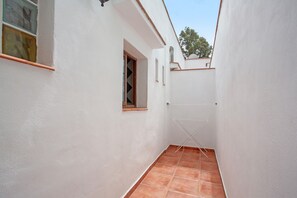 A narrow corridor with white walls, a tiled floor, a window with wooden shutters, and a clothes drying rack.