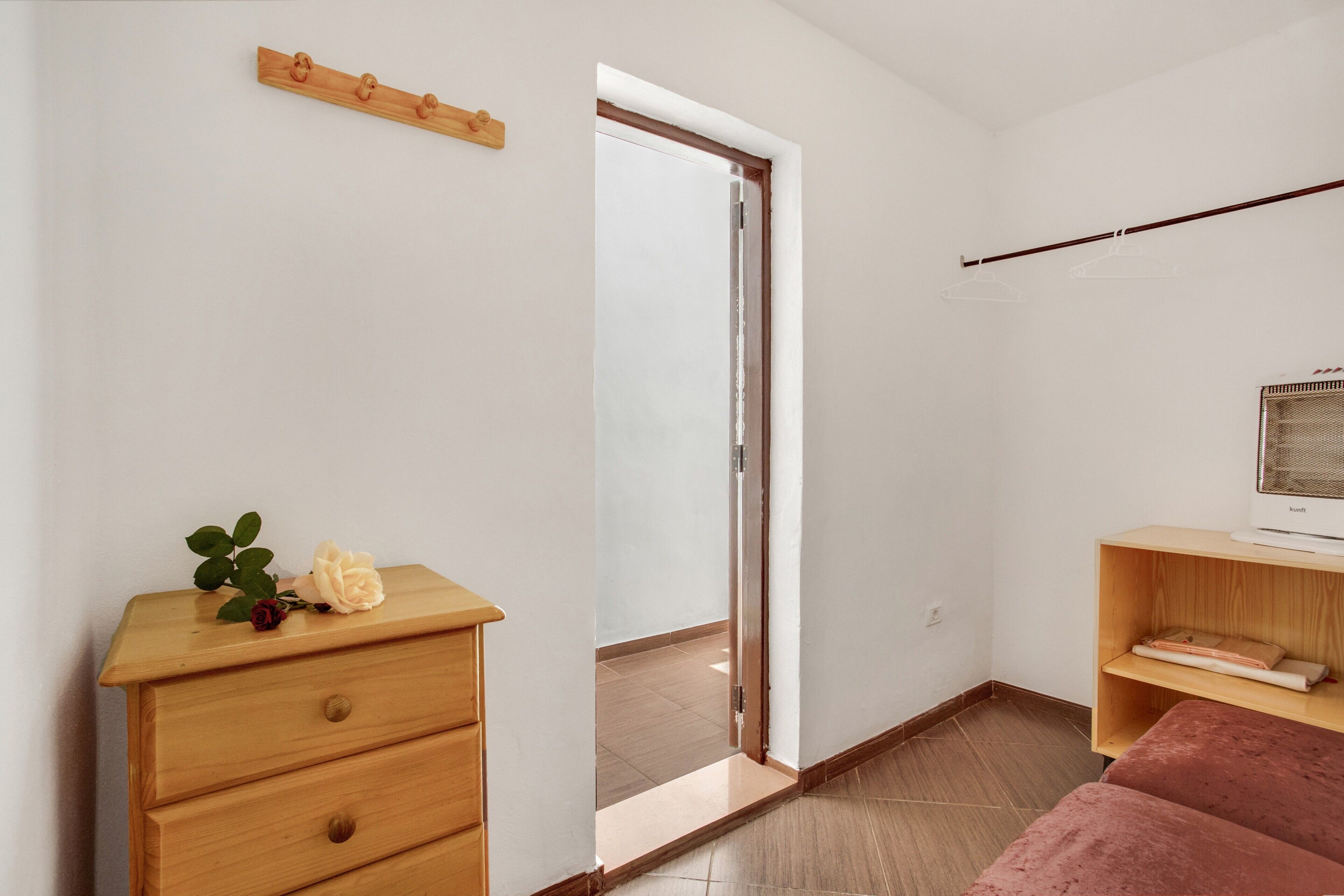 A room with a wooden dresser, a bed, a television on a wooden stand, and a door leading to an outdoor area.