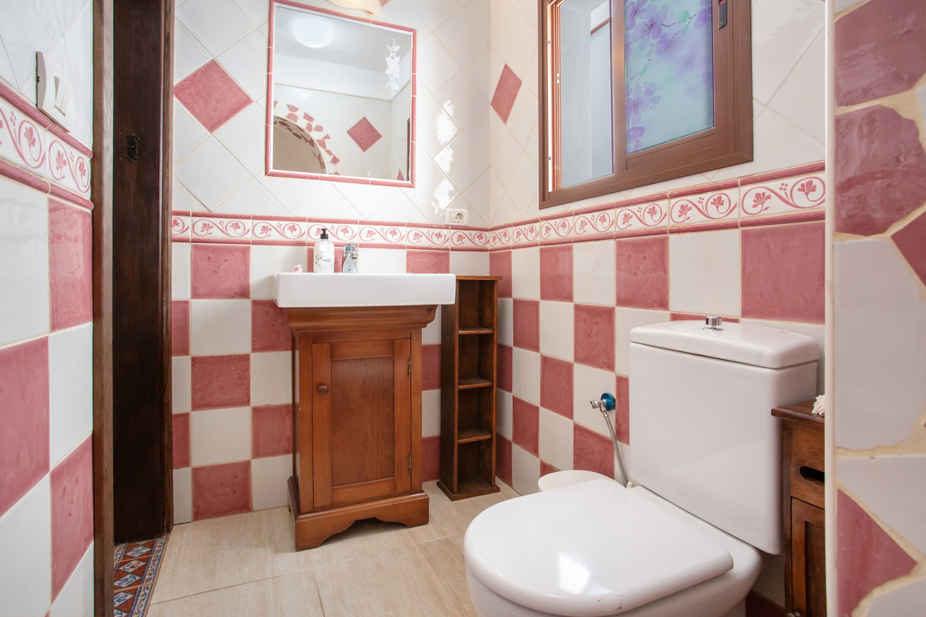 A bathroom with a white toilet, wooden cabinet, and a sink.