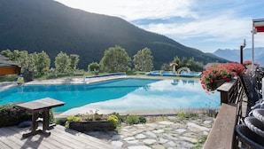 Une piscine d’un bleu éclatant, dotée d’une terrasse en bois, entourée de verdure et avec une chaîne de montagnes en toile de fond.