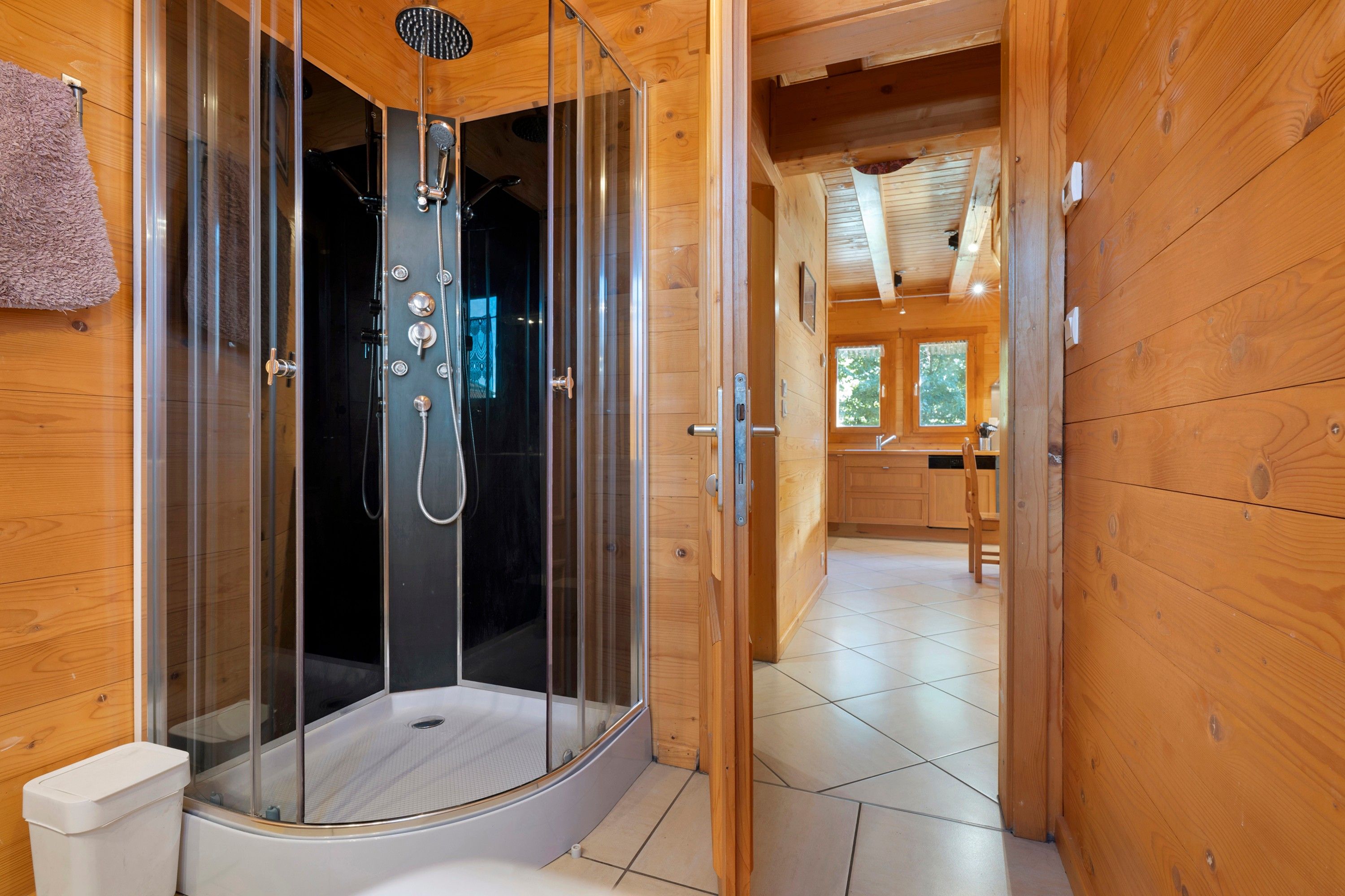 Een houten cabinestijl interieur met een douchecabine met glazen wanden, een zichtbaar toilet en een keukenhoek met houten kastjes.