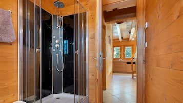 Een houten cabinestijl interieur met een douchecabine met glazen wanden, een zichtbaar toilet en een keukenhoek met houten kastjes.