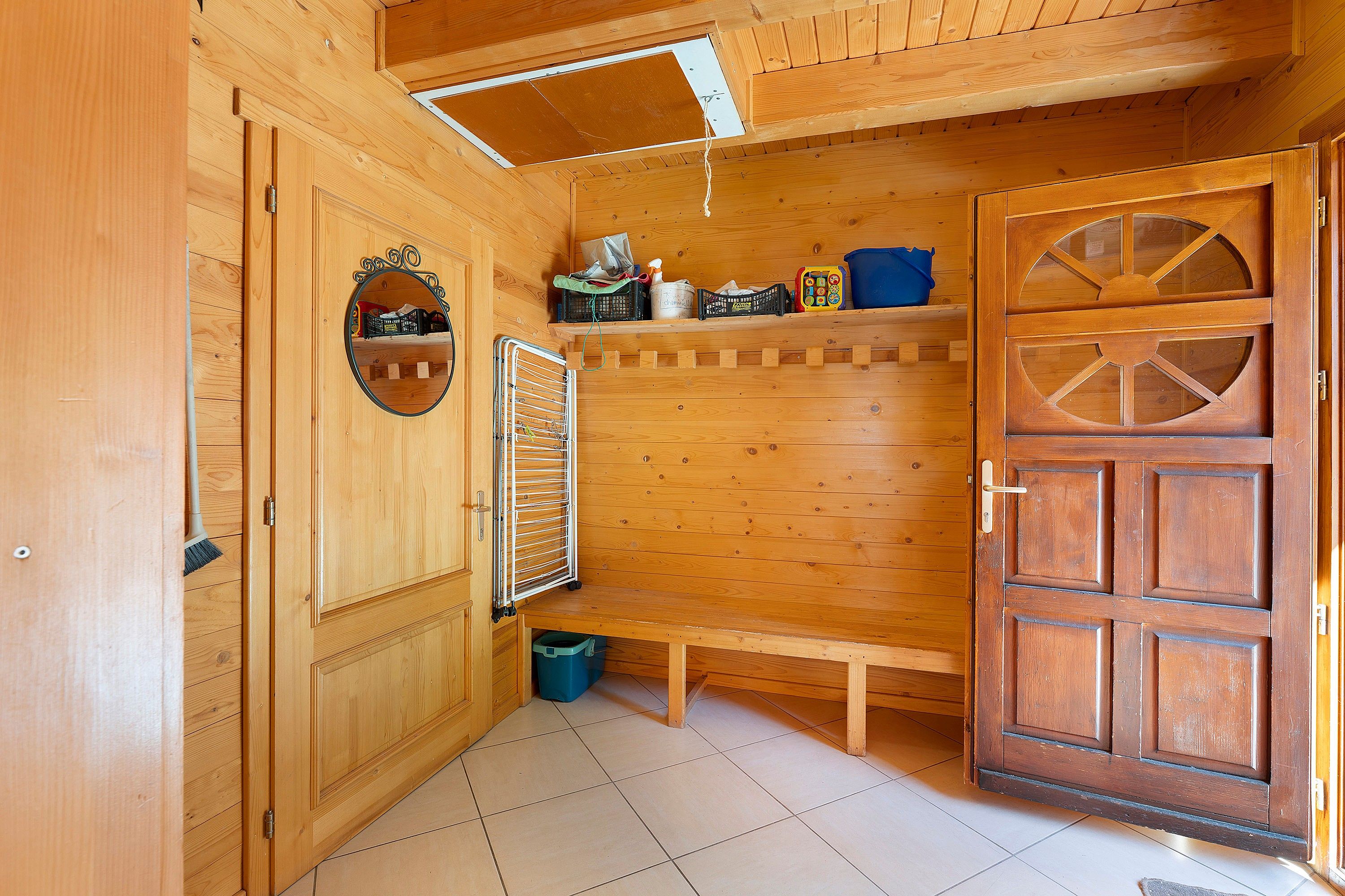 Een houten interieur met een bankje, een spiegel en een deur met ruit.