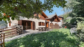 Un chalet doté d’une terrasse en bois, d’un espace salon extérieur et offrant une vue sur la verdure et les montagnes environnantes.