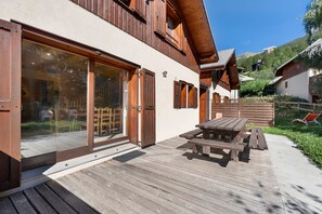 Un chalet en bois doté d’une terrasse, de portes-fenêtres coulissantes et d’une table en bois.