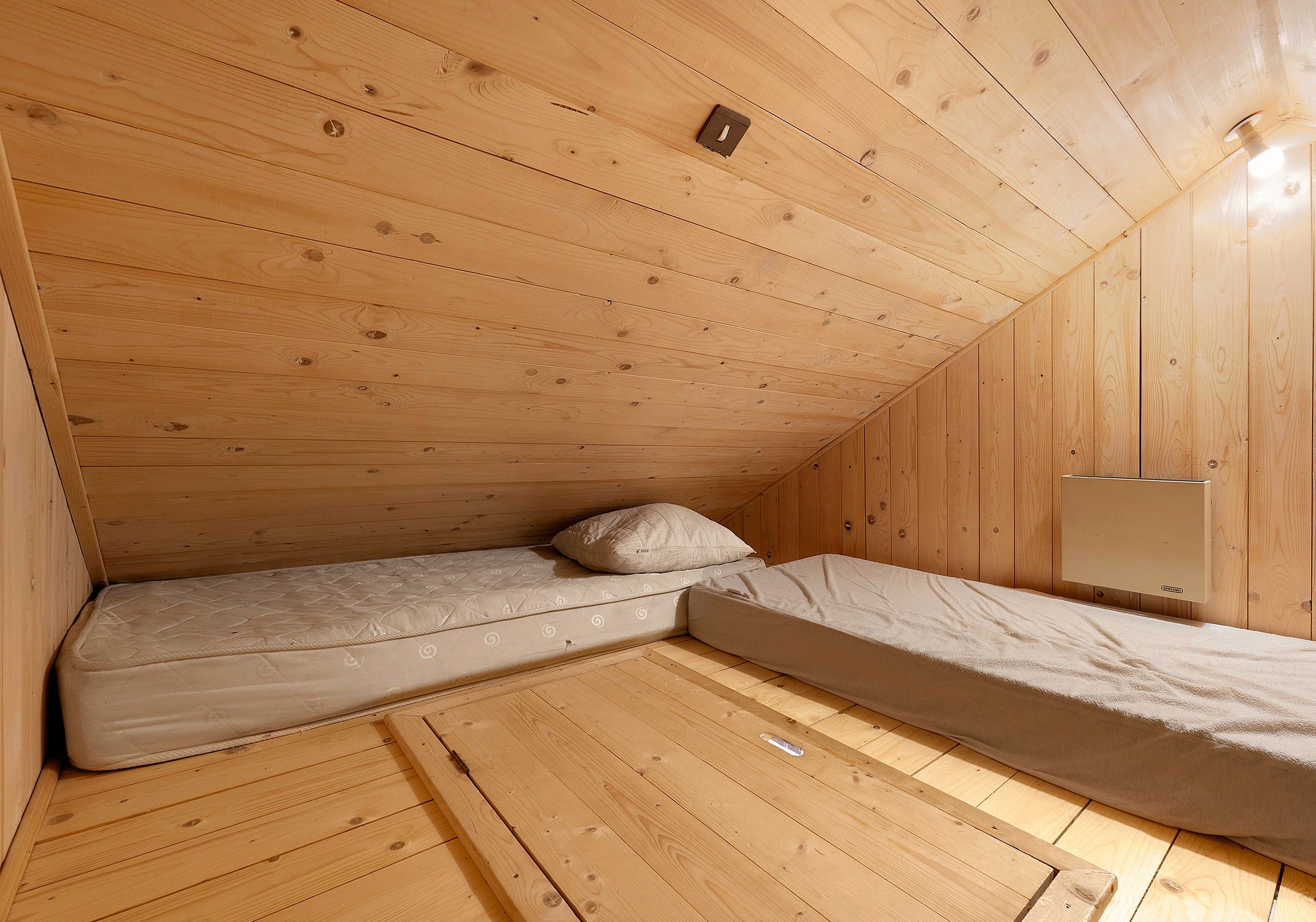 Une petite cabane en bois avec un lit simple et une banquette intégrée.