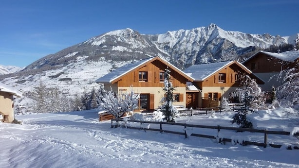 Ein Holzchalet vor einer verschneiten Landschaft und Bergen im Hintergrund.