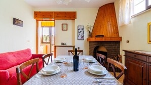 Un coin repas avec une table dressée pour quatre personnes, un canapé rouge, des chaises en bois, une cheminée en briques et une fenêtre avec des rideaux.