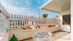 Un balcon avec une balustrade blanche, une table avec des chaises et un vase vert.
