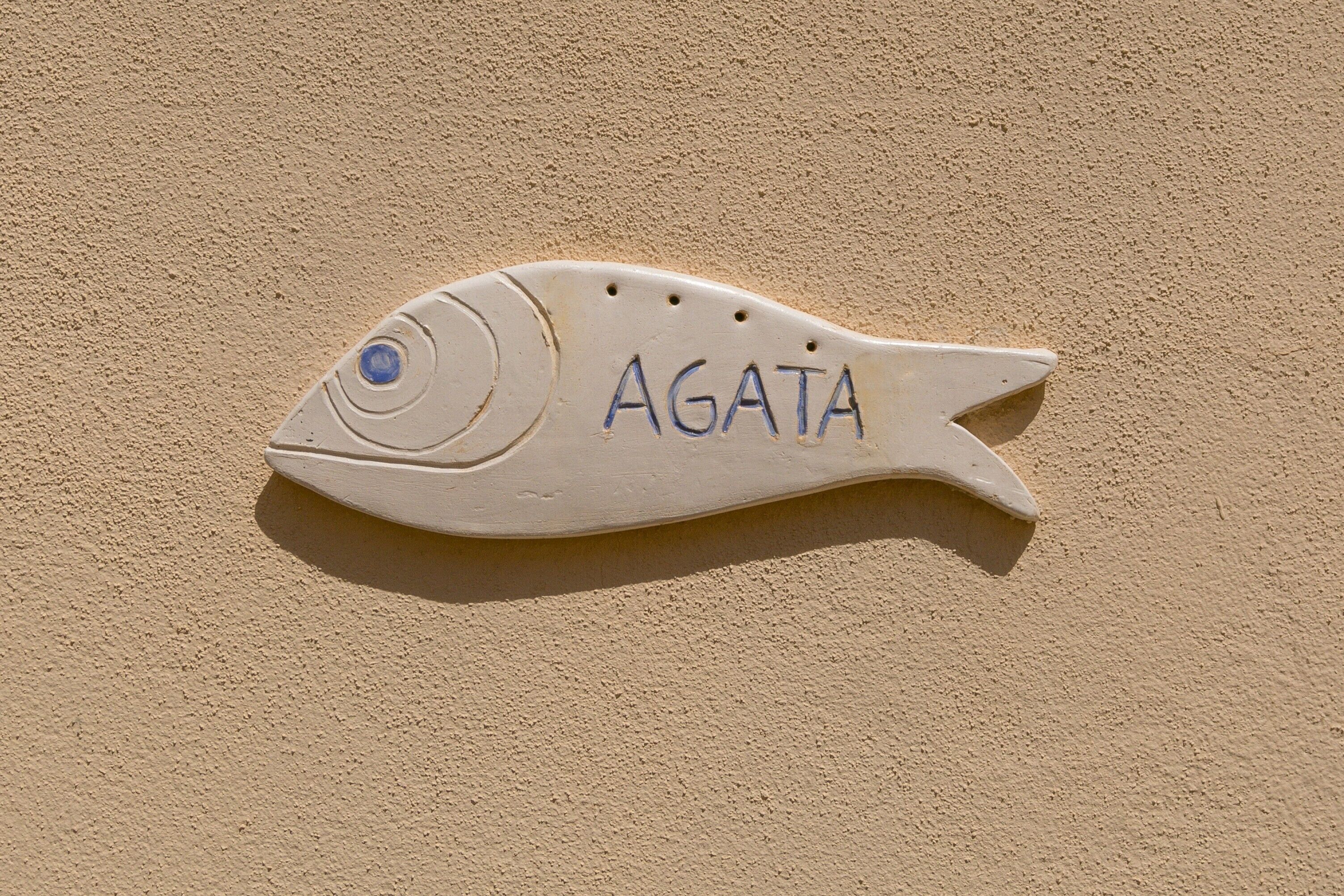 Un panneau en forme de poisson, sur lequel est inscrit le mot « AGATA », est fixé à un mur texturé.