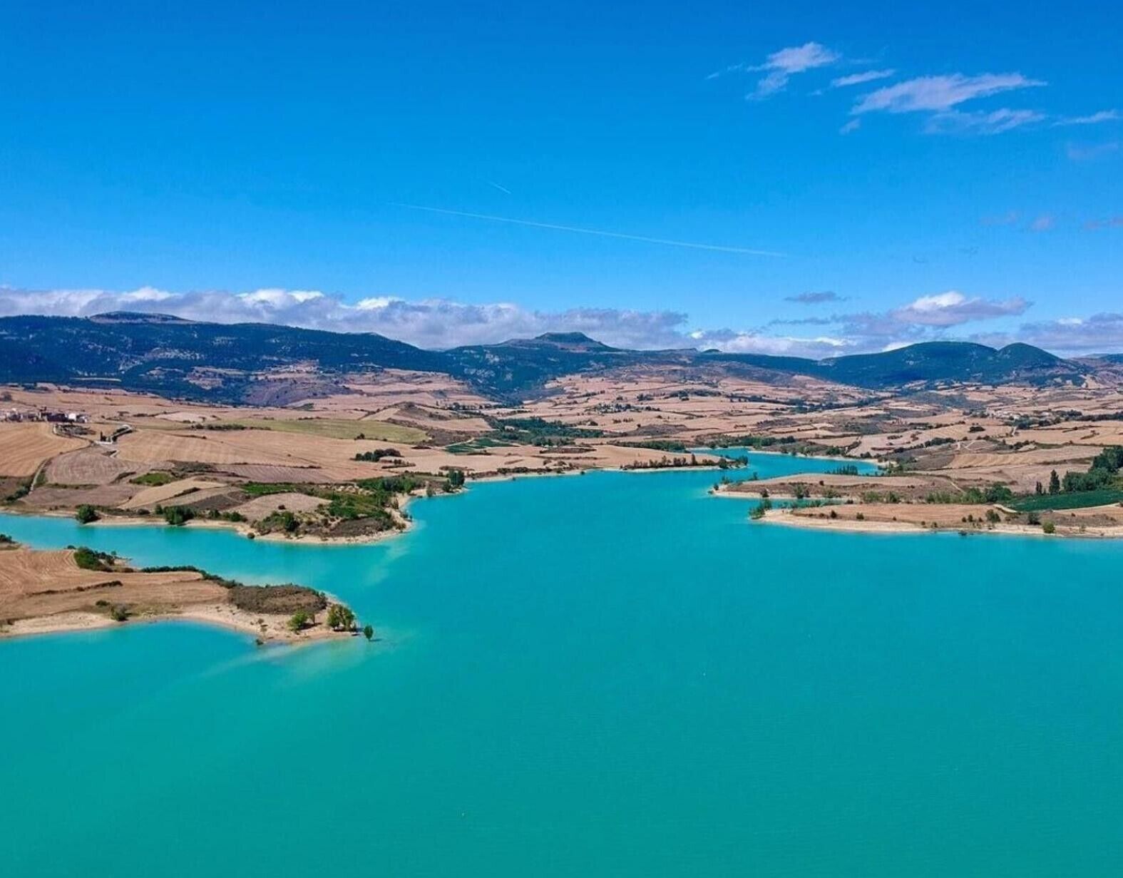 A panoramic view of a coastal landscape with turquoise waters, distant mountains, and a clear sky.