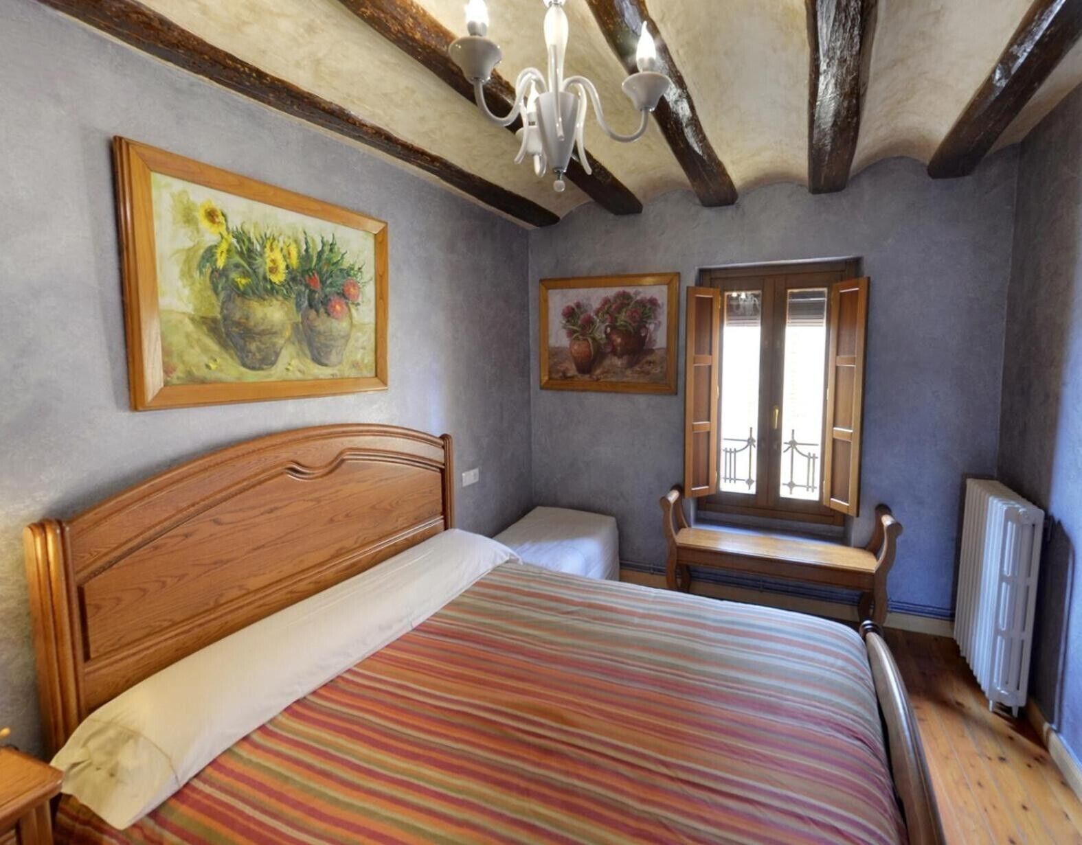 A bedroom with a wooden bed, a bench, a radiator, and two paintings on the wall.
