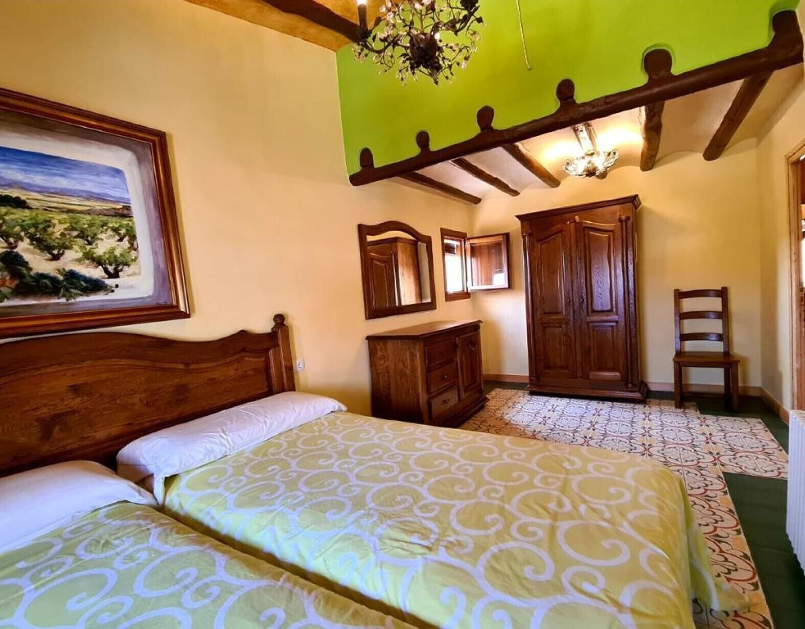 A bedroom with a bed, a wooden wardrobe, a chair, and a painting on the wall.
