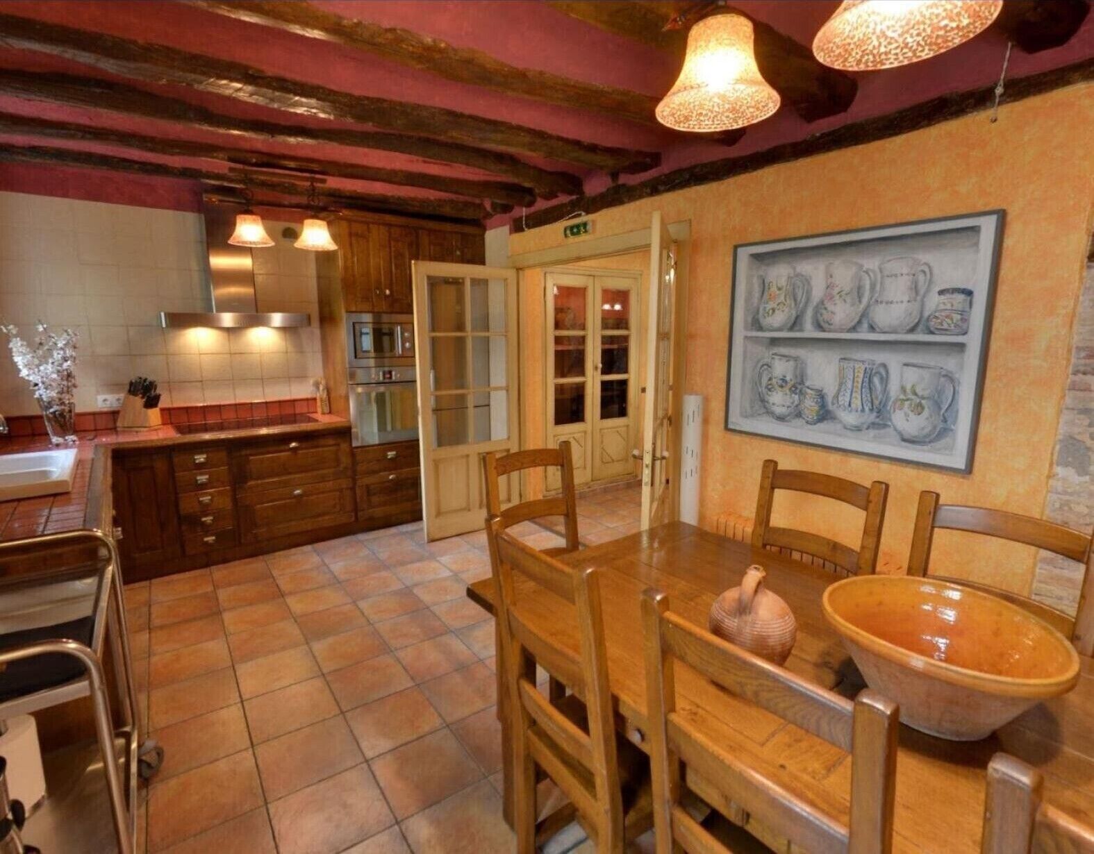 Een keuken met houten kastjes, een eettafel met stoelen, een grote keramieken kom en een wanddecoratie van keramische mokken.
