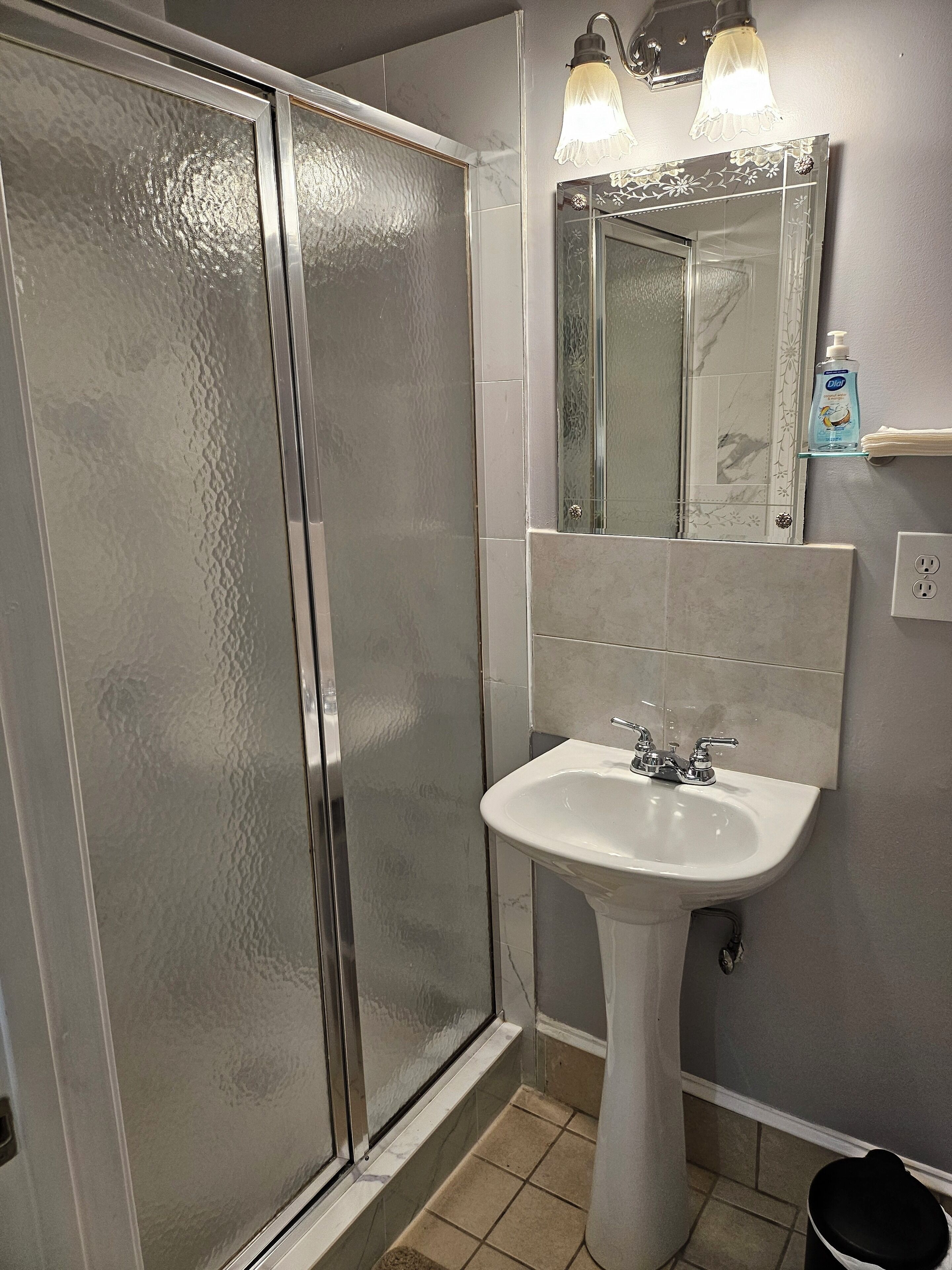 A bathroom with a glass shower enclosure, a white sink, and a mirror with a decorative frame.