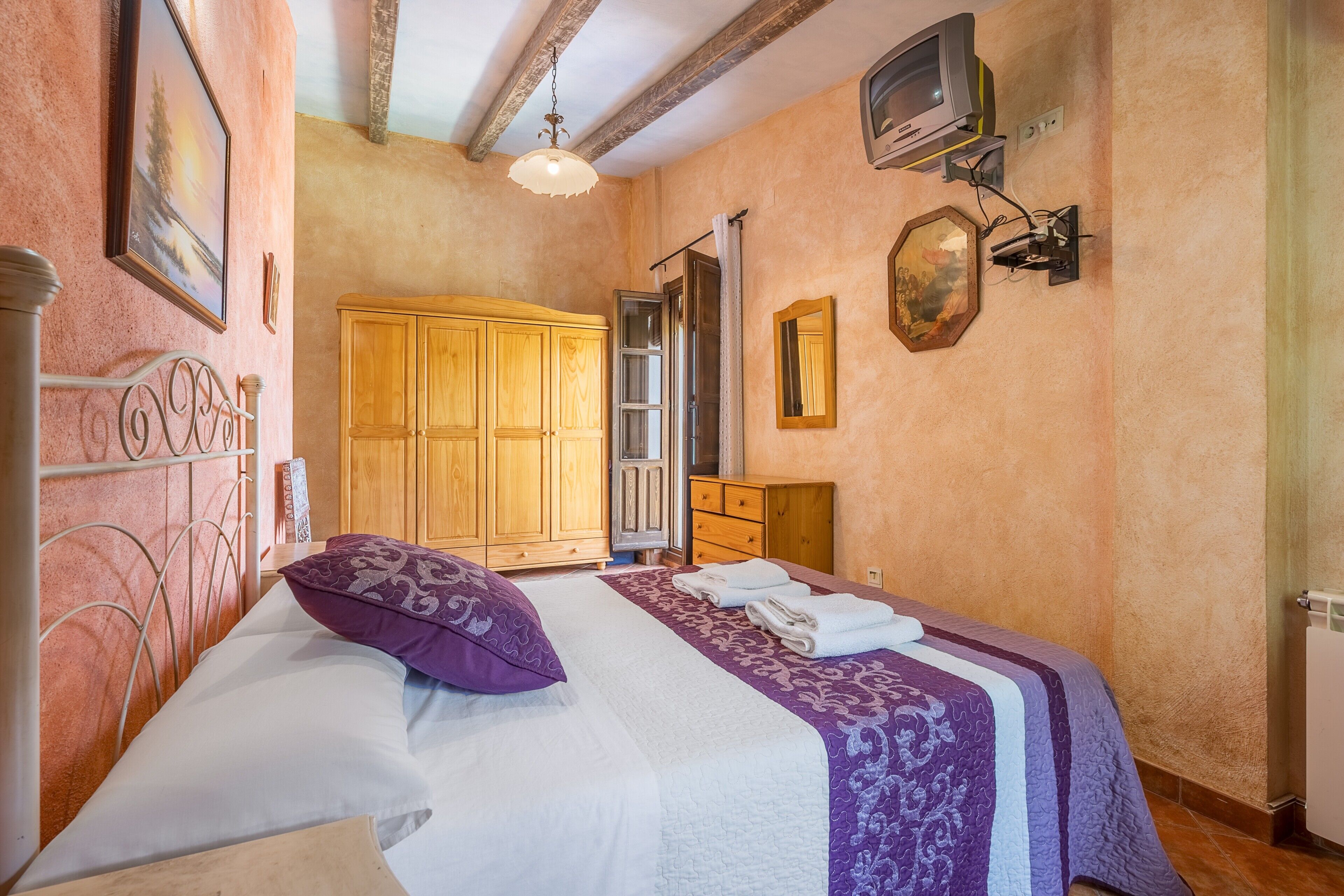 Un dormitorio con cama, armario de madera y televisión montada en la pared.