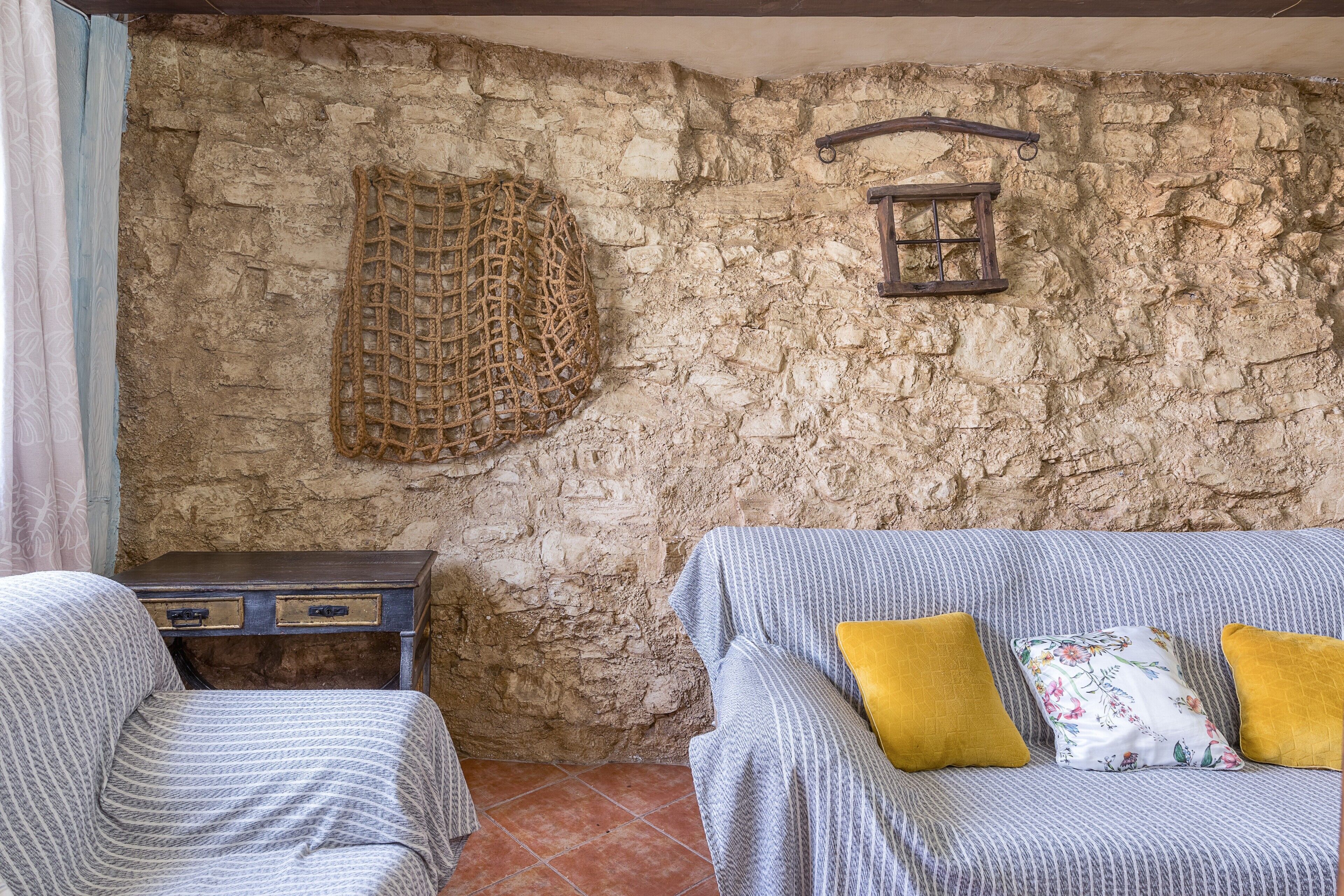 Une pièce rustique avec un mur en pierre, un panier en osier, une table de chevet en bois, un canapé à rayures et deux coussins.