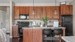 Eine moderne Küche mit Holzschränken, einer zentralen Kochinsel mit Barhocker, Edelstahlgeräten und Pendelleuchten.