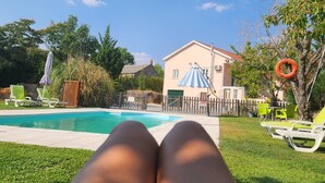 Zona de piscina con una casa al fondo, una valla y un árbol con un columpio de neumático.