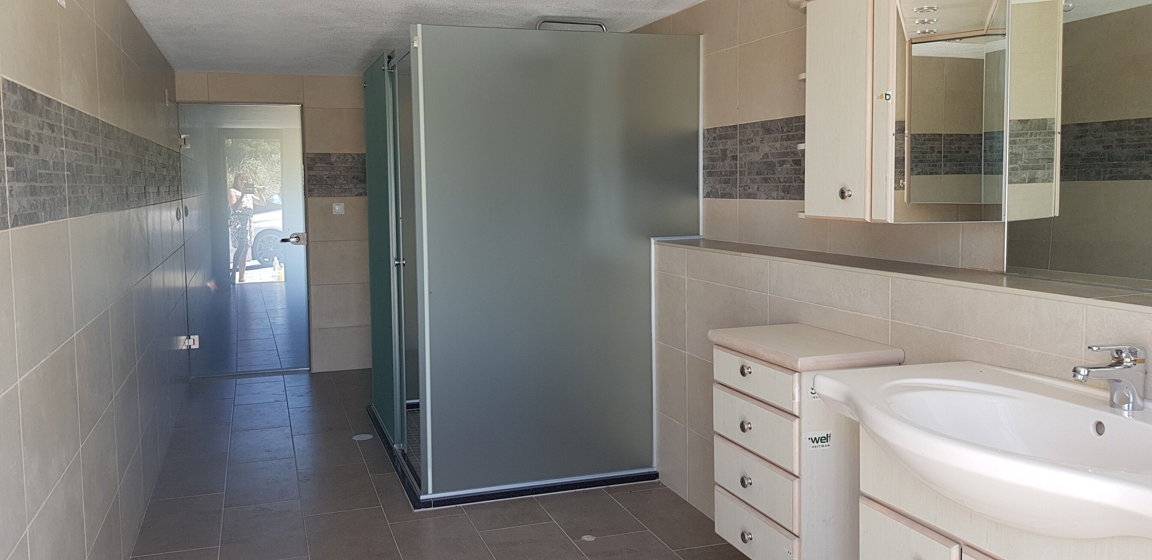 Een badkamer met een douche, wastafel en spiegel.