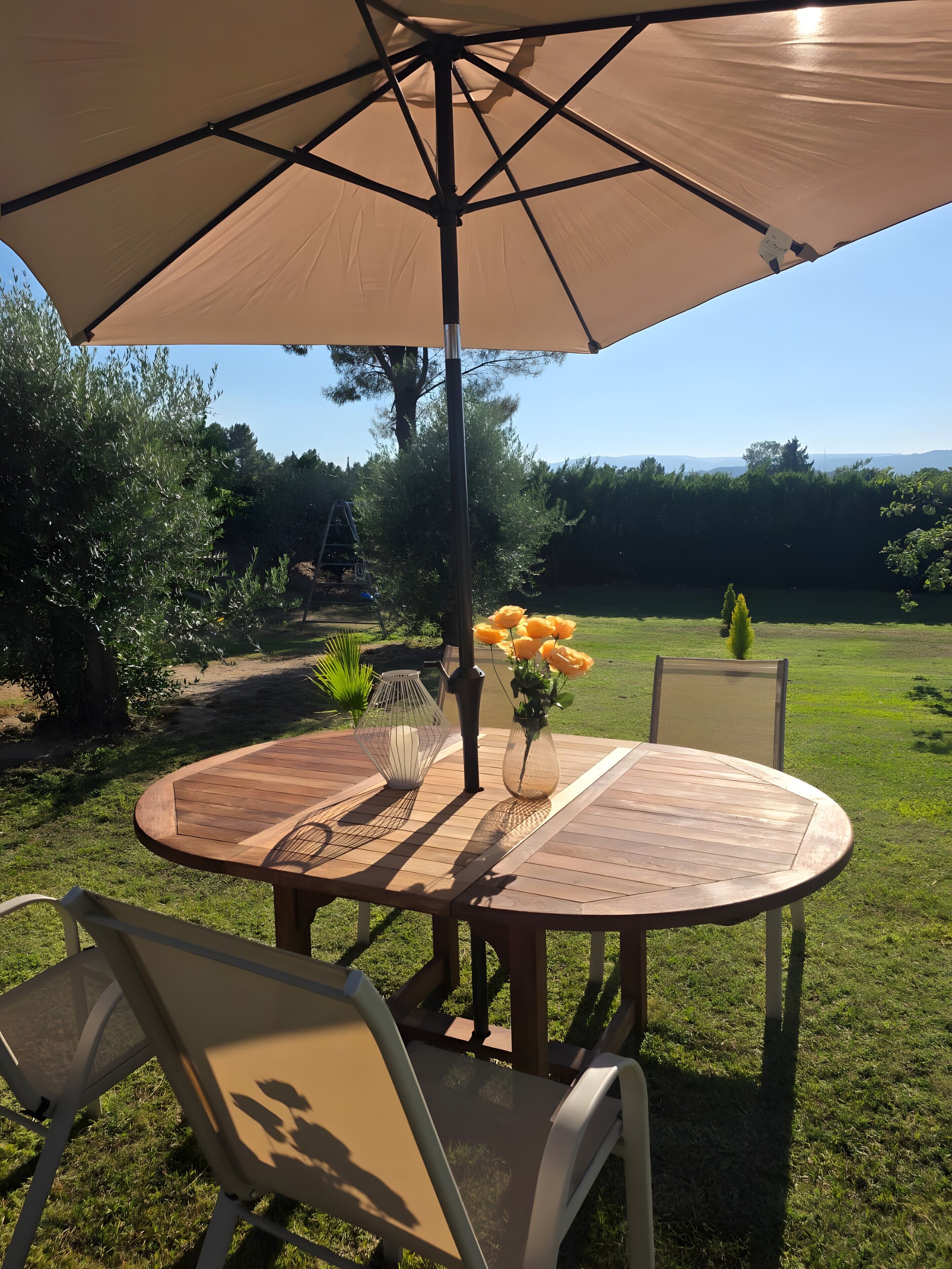 An outdoor patio with a round table, chairs, a table lamp, and a vase with flowers.