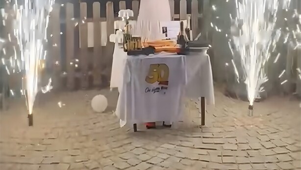 Una persona de pie con los brazos levantados frente a una mesa con varios objetos.