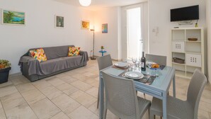 A living room with a sofa, dining table, chairs, and a TV mounted on the wall. - Apartment 'Villa Corallo - Turchese' with Shared Garden, Wi-Fi and Air Conditioning (San Vincenzo)