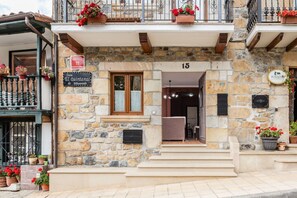 A stone building with a sign indicating it is a guesthouse, number 15, with a balcony and flower pots.
