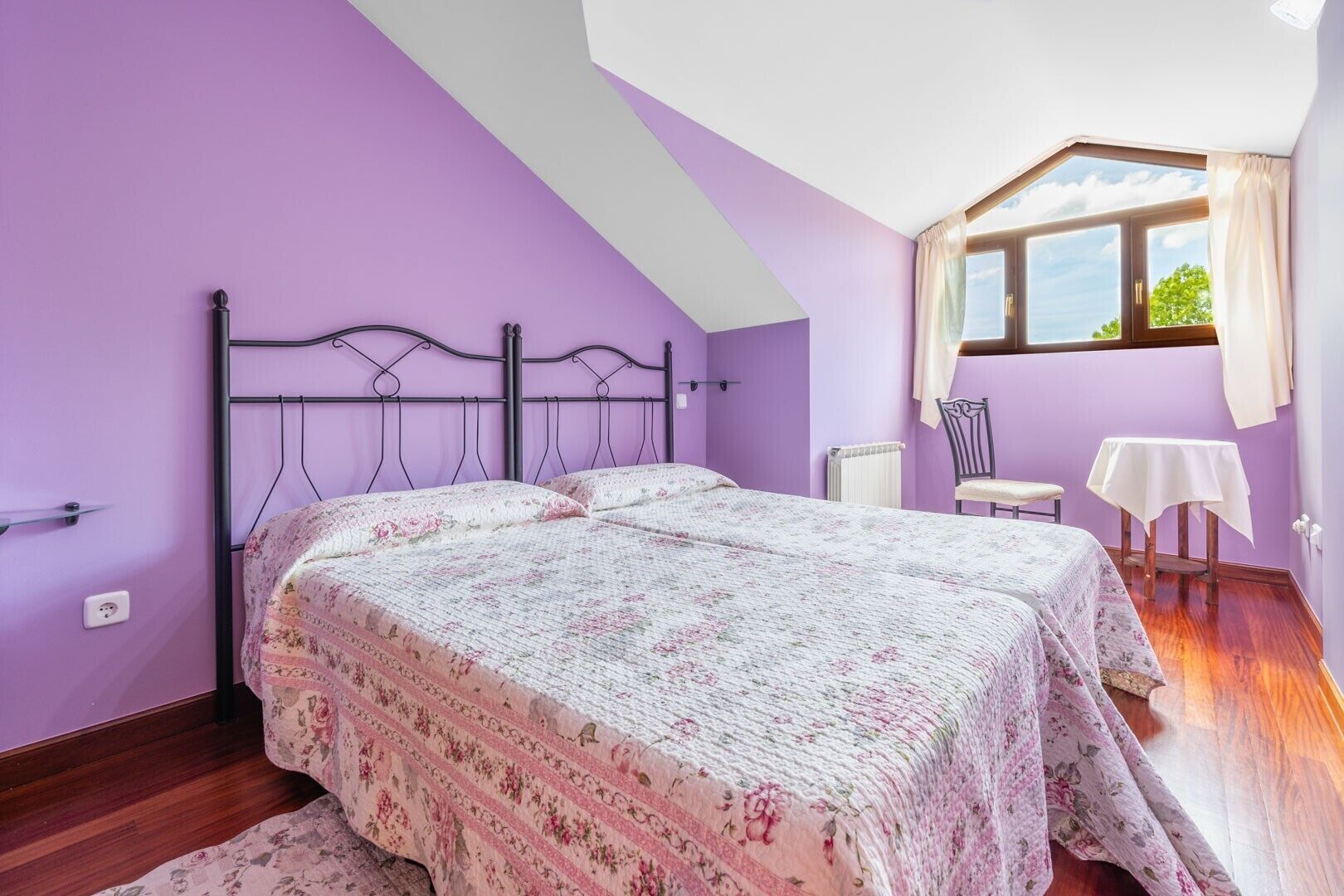 A bedroom with two beds, a window, a chair, and a small table.