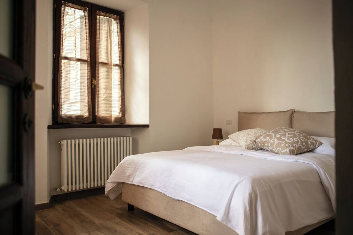A bedroom with a bed, a radiator, and a window with curtains.