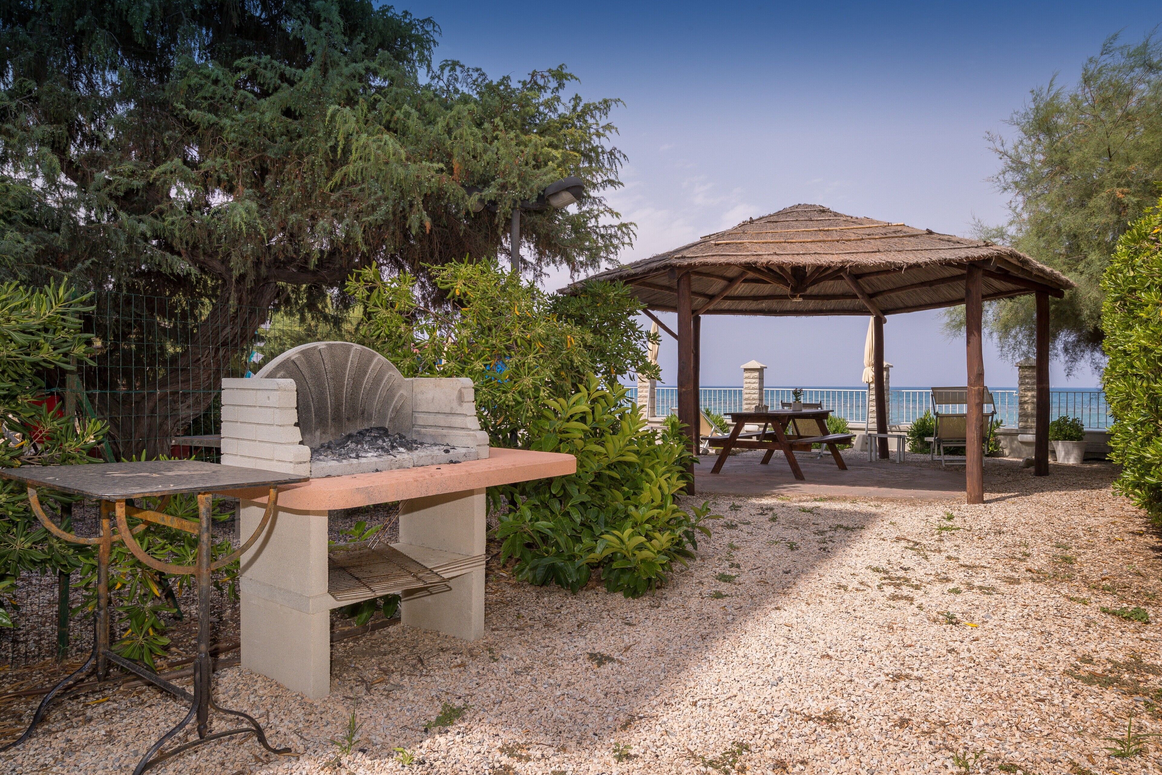 Une terrasse avec un barbecue, une table et un belvédère donnant sur un plan d’eau.