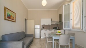 Una cocina compacta con refrigerador, microondas y estufa, una mesa de comedor con sillas, y un sofá gris.
