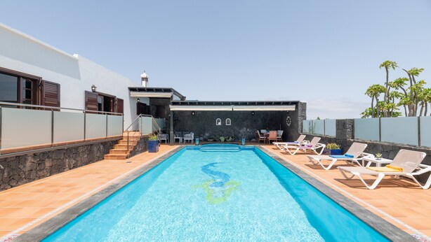 Una piscina con sillas de descanso, un muro de piedra y una escalera que lleva a un nivel superior.