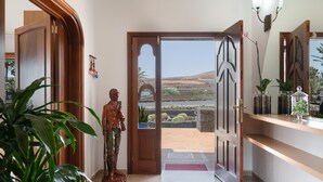 Un pasillo con una puerta de madera que da a un balcón, una estatua y una estantería con adornos.