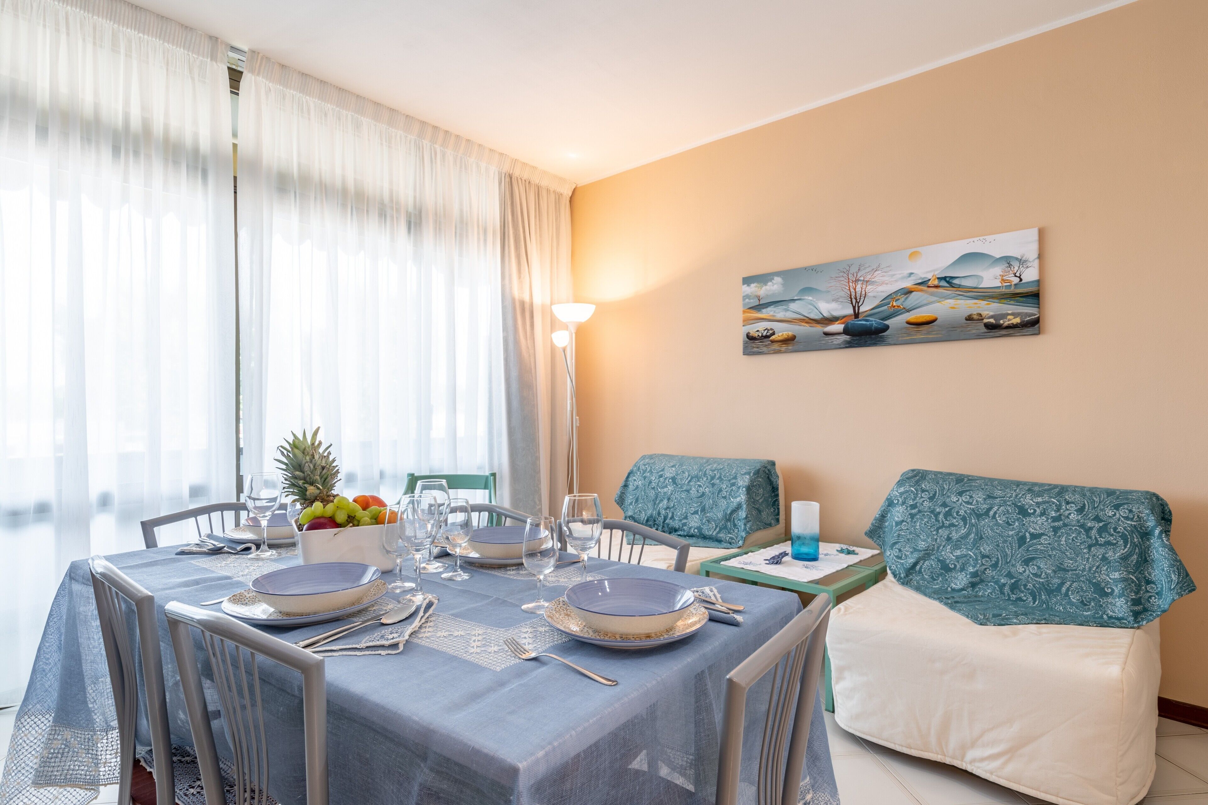 Un comedor con una mesa dispuesta para cuatro personas, un frutero y un cuadro en la pared.