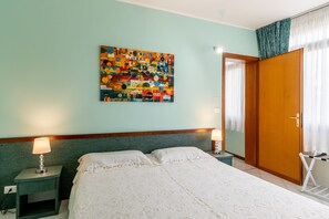 A bedroom with a bed, two bedside tables with lamps, a colorful abstract painting on the wall, a wooden wardrobe, and a window with curtains. - Apartment 'Casa Vacanza Marina Di Pietrasanta' with Mountain View, Wi-Fi and Air Conditioning (Pietrasanta)