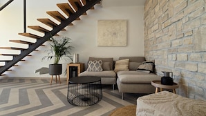 Una sala de estar moderna con una escalera, un conjunto de sofás, una mesa de centro y una planta en maceta.
