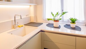 A modern kitchen with a white countertop, a stainless steel faucet, and two potted plants on the windowsill. - 605A Residenza Gigli (Garda)