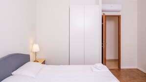 A neatly made bed with white linens and a grey headboard, a bedside lamp, and a wooden door leading to a hallway. - 605A Residenza Gigli (Garda)